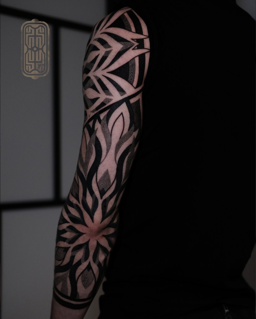 Detailed black and grey geometric tattoo design on a person's forearm, showcasing intricate patterns and shapes.