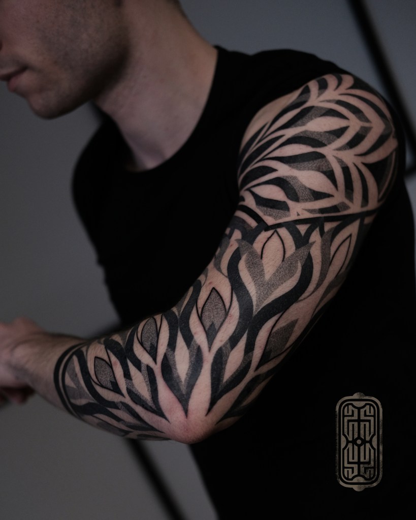 Close-up of a black tattoo design on a person's arm featuring intricate leaf patterns.