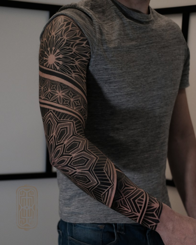 Geometric fullsleeve tattoo with patterns and mandalas.